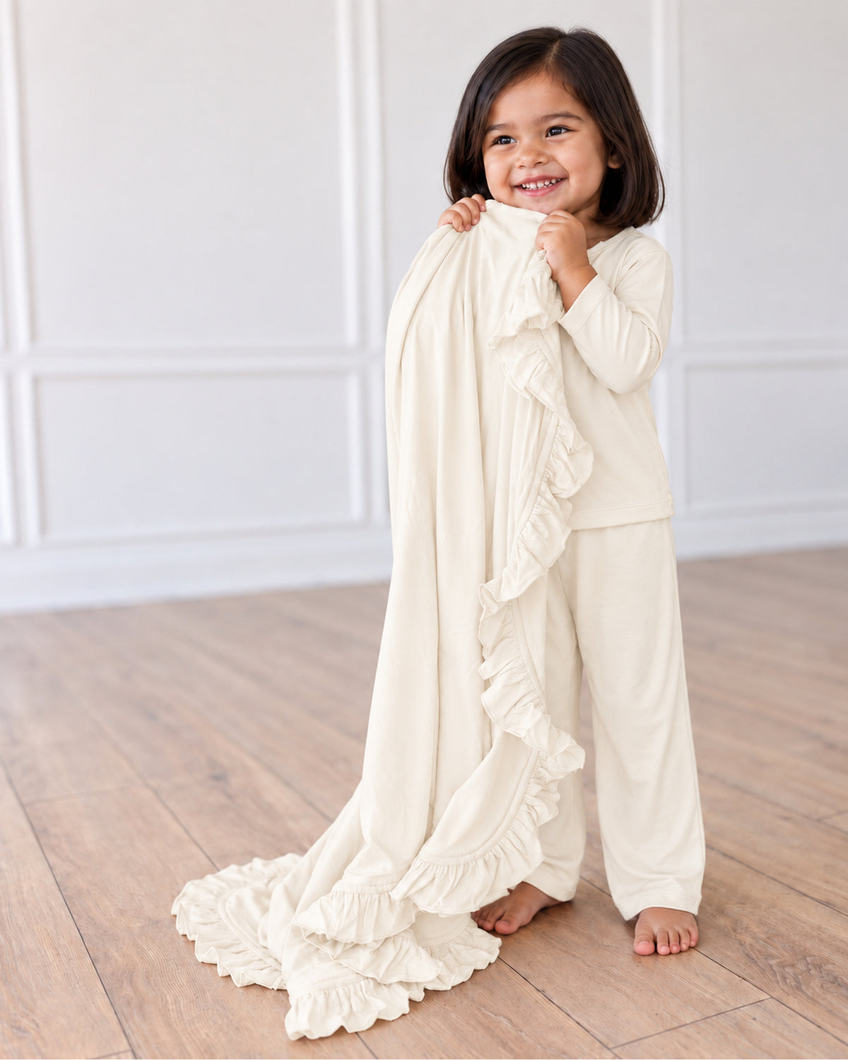 Natural色のフリルブランケットを持つ裸足の子ども。日本向けパジャマ上下セットを着用。