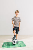Portabella Soccer柄の半袖クルーネックTシャツを着てサッカーボールに足を添える子どもの全身