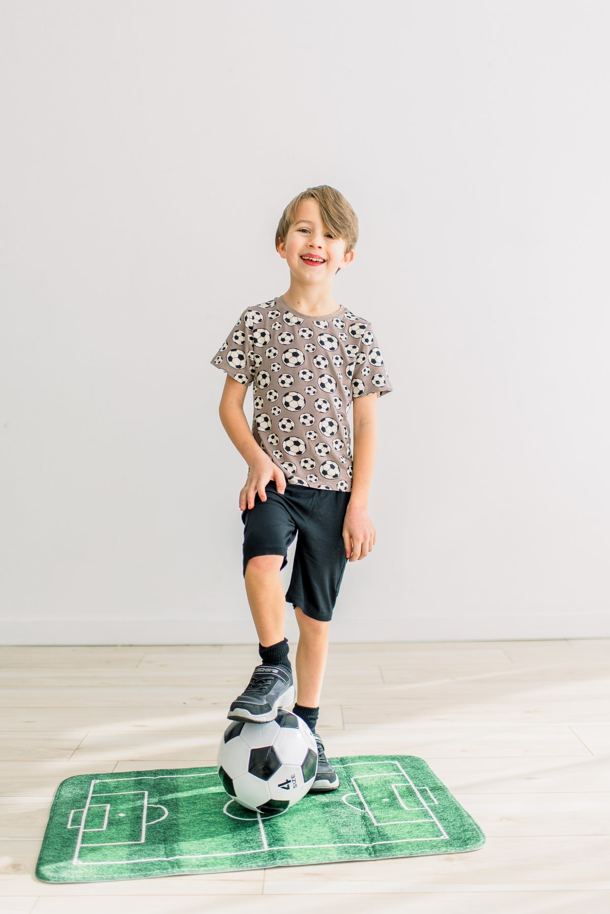 Portabella Soccer柄の半袖クルーネックTシャツを着てサッカーボールに足を添える子どもの全身