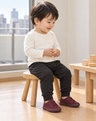 ミッドナイトのデイリージョガーパンツを着て、室内の椅子に座り木のおもちゃを持つ子ども。