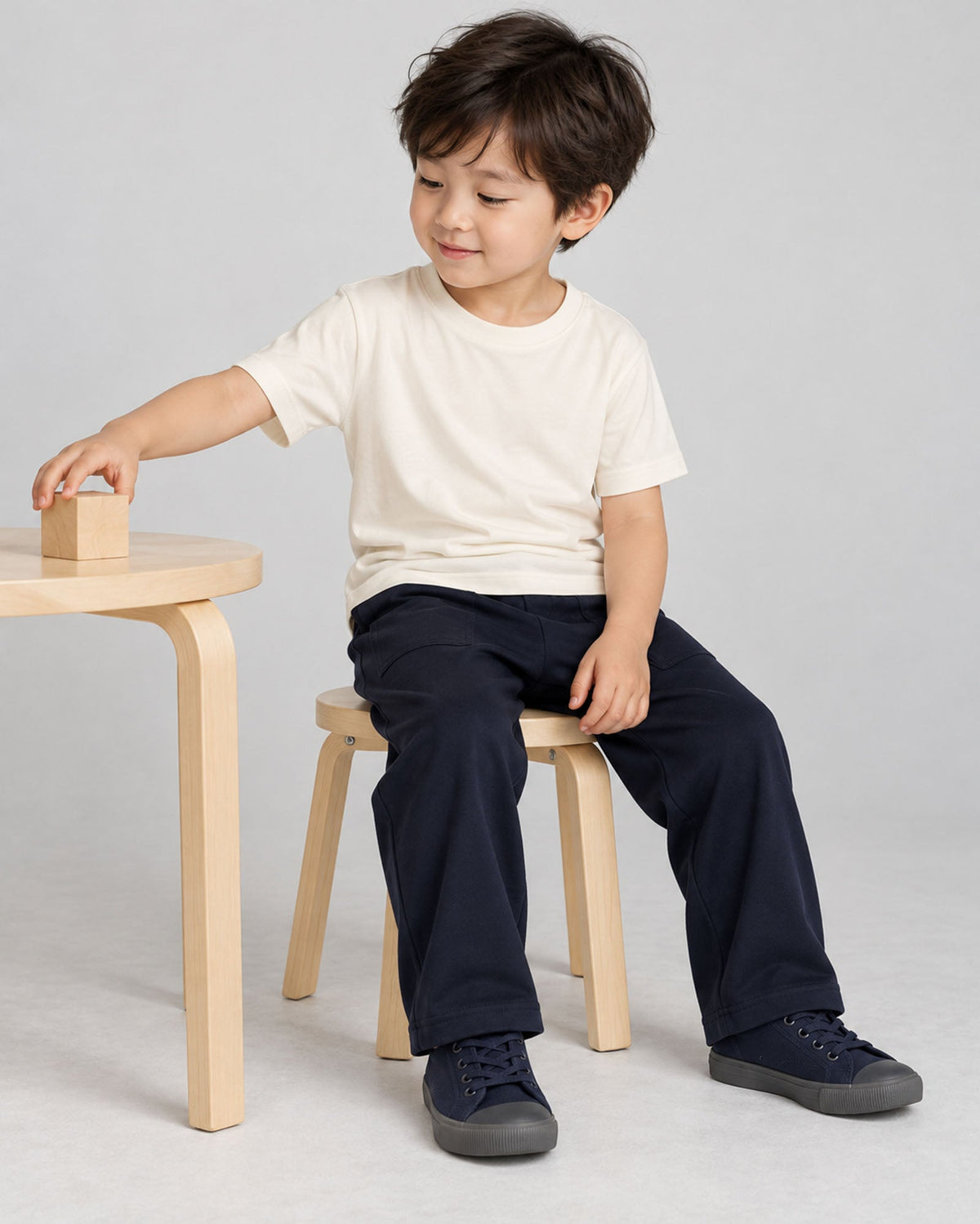 Naturalの半袖クルーネックTシャツを着て、椅子に座り木の積み木で遊ぶモデル