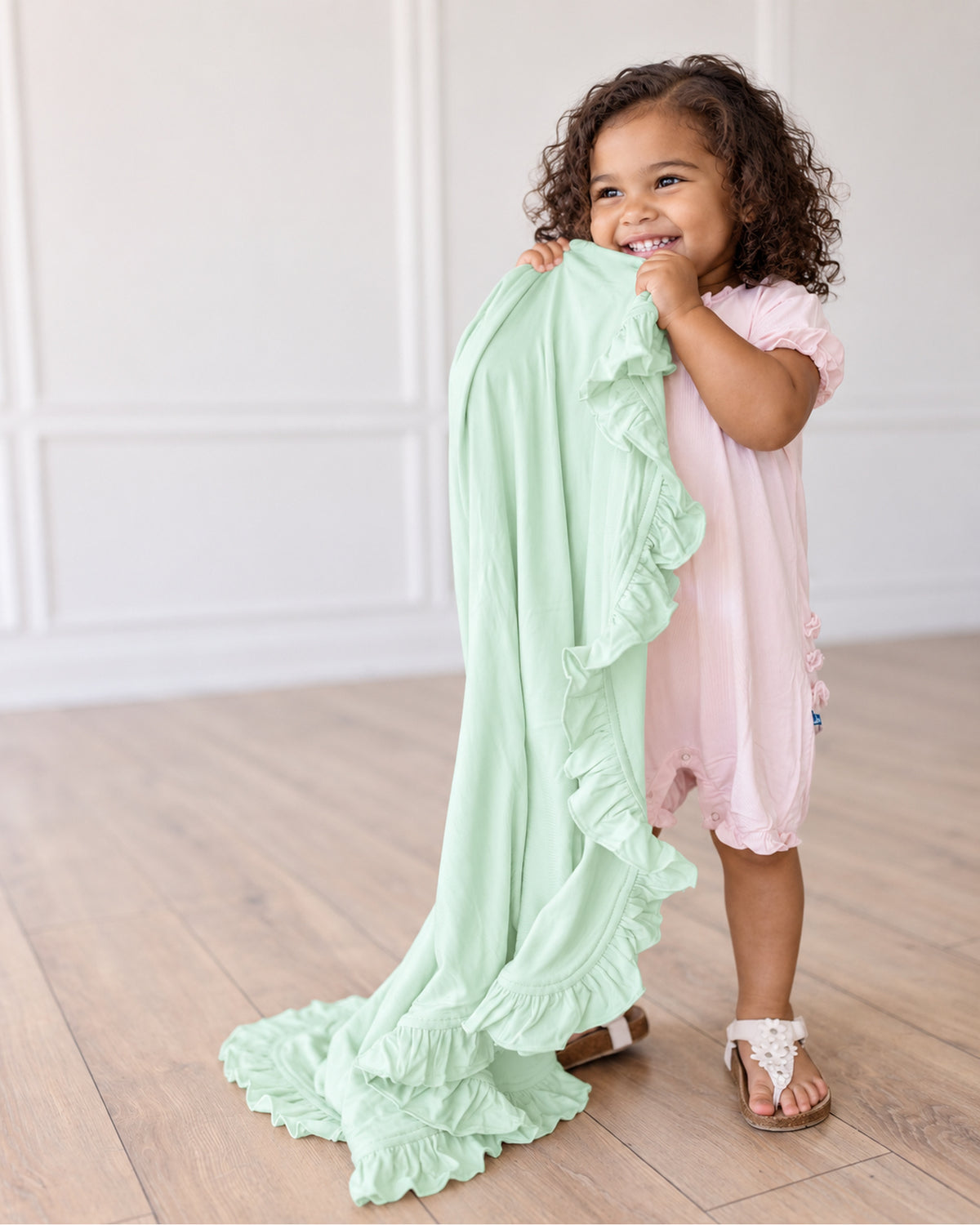 ピスタチオ色のフリルブランケットを持つ子どものイメージ。